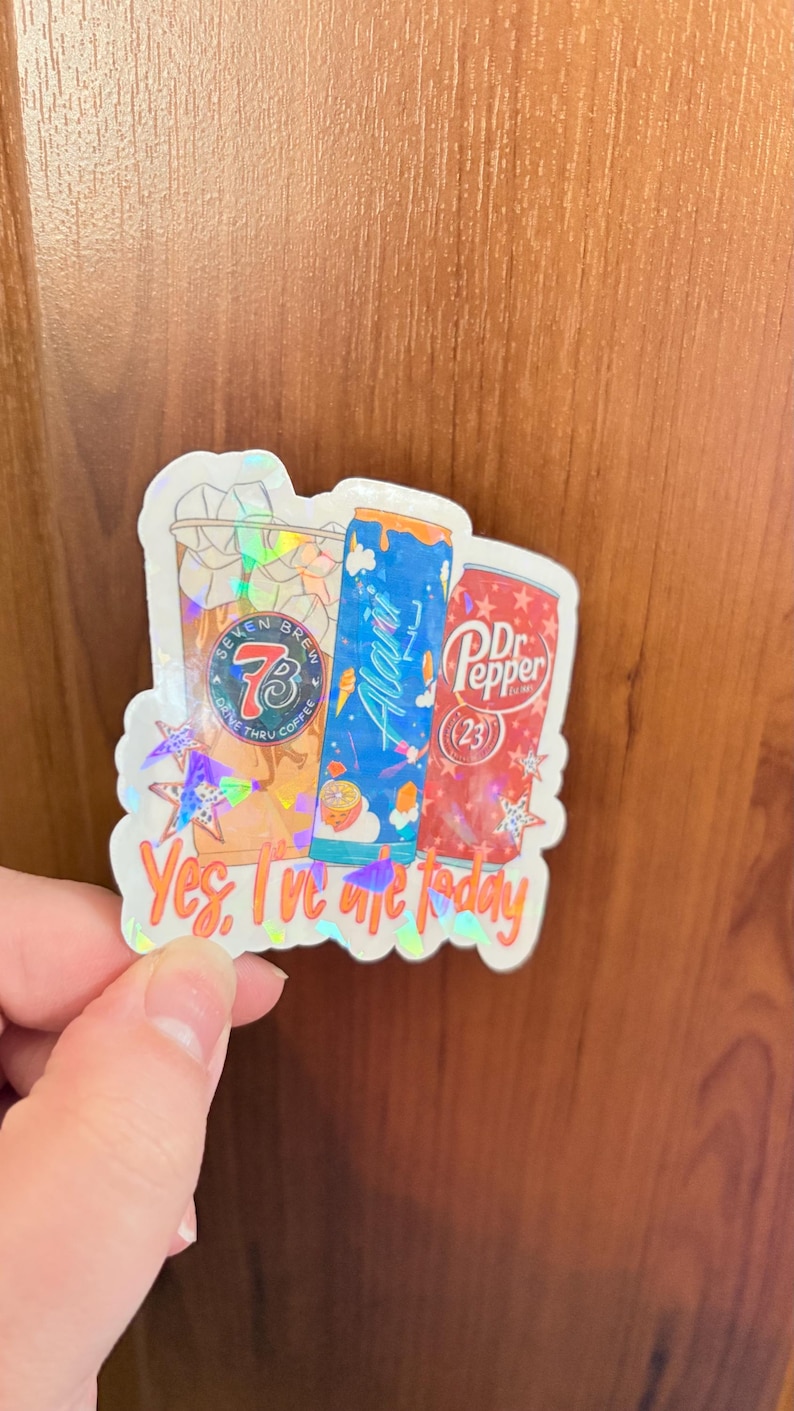May include: A holographic sticker featuring a Seven Brew coffee cup, a blue Alani Nu energy drink can, and a red Dr. Pepper can. The sticker includes the text "Yes, I've ate today" in orange script at the bottom, accented with small holographic stars.