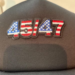 May include: Black baseball cap with the embroidered numbers "45/47" in a patriotic design. The numbers are outlined in black and feature red, white, and blue colors, with the "4" and "7" having a star pattern.