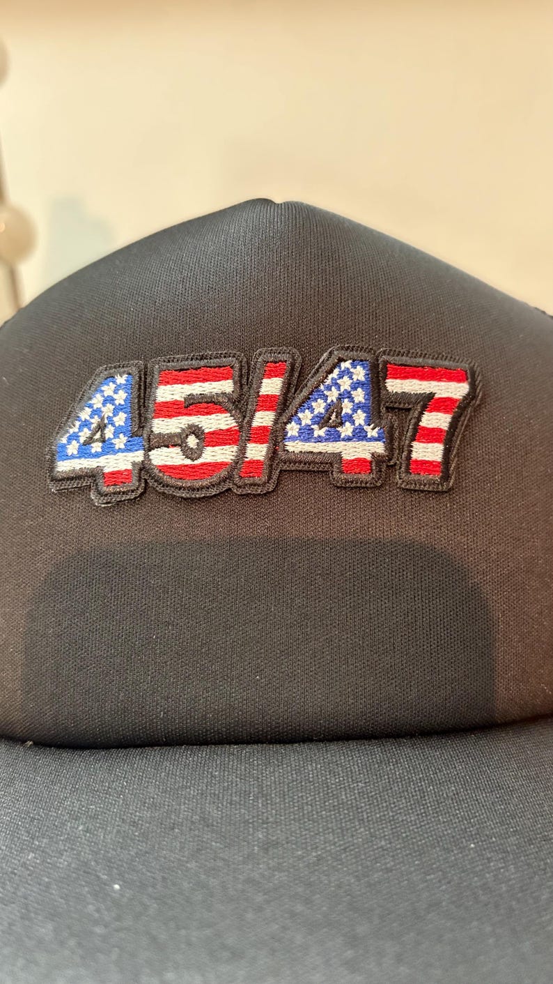 May include: Black baseball cap with the embroidered numbers "45/47" in a patriotic design. The numbers are outlined in black and feature red, white, and blue colors, with the "4" and "7" having a star pattern.