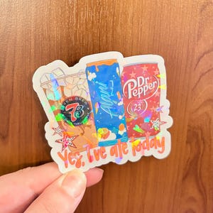 May include: A holographic sticker featuring a Seven Brew coffee cup, a blue Alani Nu energy drink can, and a red Dr. Pepper can. The sticker includes the text 'Yes, I've ale today' in orange script at the bottom, accented with small star shapes.