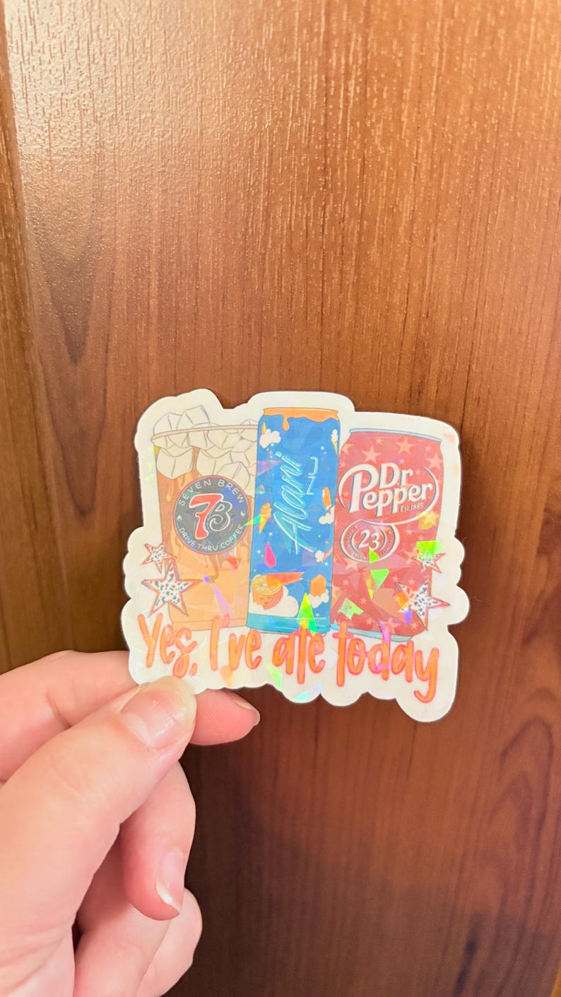 May include: A holographic sticker featuring three beverage containers: a Seven Brew iced coffee, an Alani Nu energy drink, and a Dr. Pepper can. The sticker is decorated with star shapes and includes the text "Yes, I've ate today" in orange lettering.