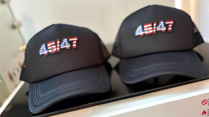 May include: Two black trucker hats with the text "45/47" in red, white, and blue, resembling the American flag. The hats have a curved brim and a mesh back.