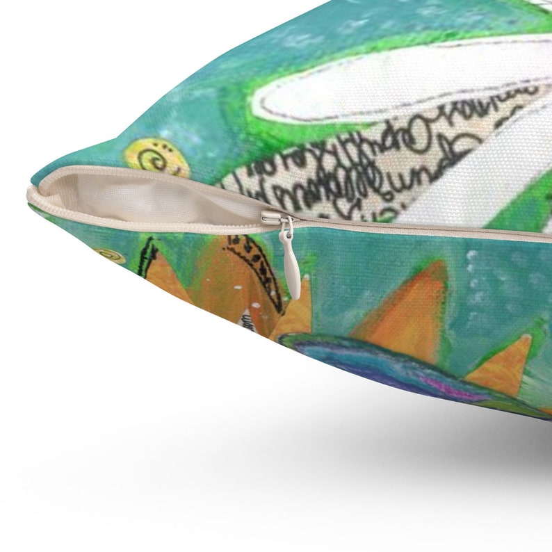 May include: A teal blue pillow with a zipper closure. The pillow features a colorful abstract design with a yellow crown and a white cloud with handwritten text. The text reads "I'd rather be the crown than the one who wears it".