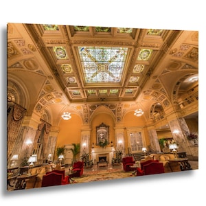 May include: An ornate interior featuring a high ceiling with stained glass panels and decorative molding. The room has a fireplace, red armchairs, and a patterned rug, creating a luxurious and elegant atmosphere. The walls are painted in a warm yellow color.