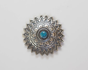 May include: A silver and turquoise concho with a detailed floral design. The concho has a starburst shape with a central turquoise stone.