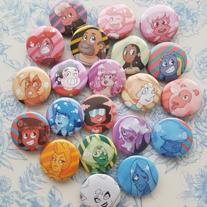 Peut inclure: Un ensemble de 18 boutons ronds colorés représentant des personnages de la série télévisée d'animation Steven Universe. Les boutons présentent divers personnages, dont Steven, Garnet, Amethyst, Peridot, Lapis Lazuli, et bien d'autres. Chaque bouton a un design et une palette de couleurs différents.