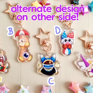 May include: Five colorful character keychains with gold star-shaped charms. The characters are a knight, a jester, a masked figure, a character with an umbrella, and a character with a crown. The keychains are on a wooden surface with origami stars.