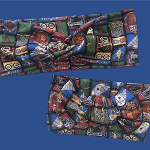 May include: Two colorful fabric headbands with a Harry Potter theme. The headbands are made of a soft, stretchy fabric and feature a variety of Hogwarts house crests and symbols. The headbands are tied in a knot at the top.