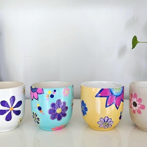 May include: Four ceramic flower pots with different floral designs. The pots are white with blue, yellow, pink, and turquoise flowers.