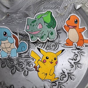 Könnte beinhalten: Vier gestickte Bügelbilder mit beliebten Pokémon-Charakteren: Squirtle, Bisasam, Glumanda und Pikachu. Die Patches sind farbenfroh und detailliert und eignen sich perfekt, um Kleidung, Taschen oder anderen Accessoires einen Hauch von Nostalgie zu verleihen.