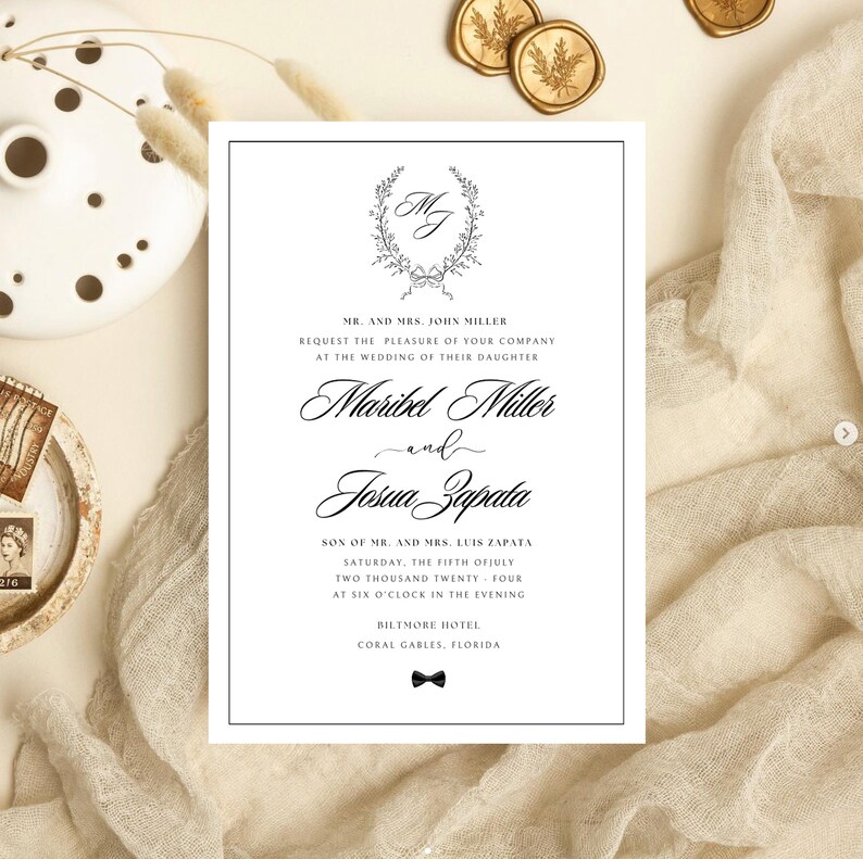 Puede incluir: Invitaci&oacute;n de boda elegante con borde negro. Presenta una corona floral con las iniciales "MJ" y los nombres "Maribel Miller" y "Josua Zapata". La invitaci&oacute;n incluye los detalles de la boda y un lazo en la parte inferior.