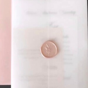 Puede incluir: Un conjunto de invitaciones de boda con una invitaci&oacute;n blanca, un sello de cera rosa claro con un dise&ntilde;o de ramita y un sobre rosa. El dise&ntilde;o es sencillo y cl&aacute;sico, creando una est&eacute;tica delicada y elegante.