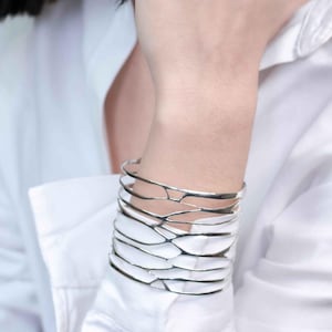 A woman in a white shirt showcases a silver cuff bracelet with a branch-inspired design, highlighting its elegant style.