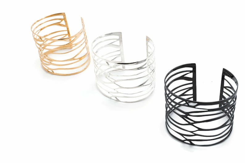 Three cuff bracelets 'Branching' with unique designs: polished silver, black-plated silver, and brass, featuring a branch-inspired motif.
