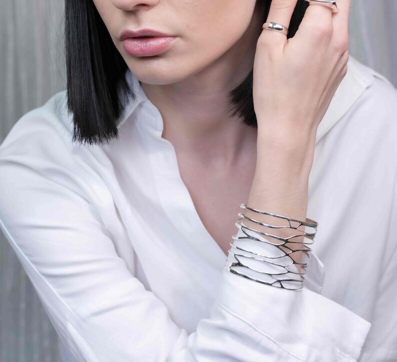 A woman in a white shirt models a silver cuff bracelet with intricate branch details, ideal for a standout accessory or gift.
