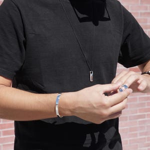 A man in a black shirt and watch, showcasing a minimalist silver Bar Necklace as a stylish accessory.