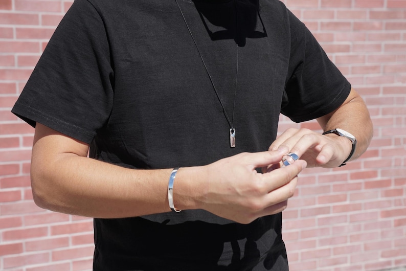 A man in a black shirt and watch, showcasing a minimalist silver Bar Necklace as a stylish accessory.