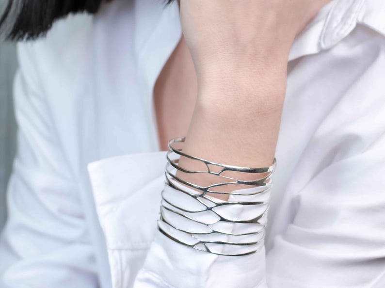 A woman in a white shirt showcases a silver cuff bracelet with a branch-inspired design, highlighting its elegant style.