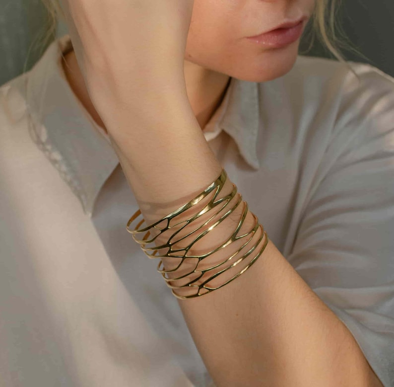 A woman models a  brass wide cuff bracelet with sculptural branch-inspired design, balancing strength and femininity.Gift idea for women.