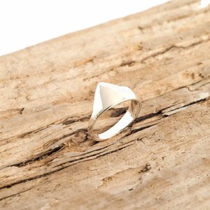 Puede incluir: Un anillo de plata con una parte superior de forma triangular. El anillo está sobre una pieza de madera desgastada.
