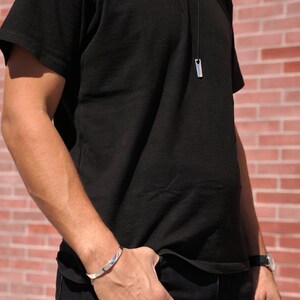 A man wearing a black shirt and jeans, showcasing a stylish polished silver bar necklace as a modern accessory.