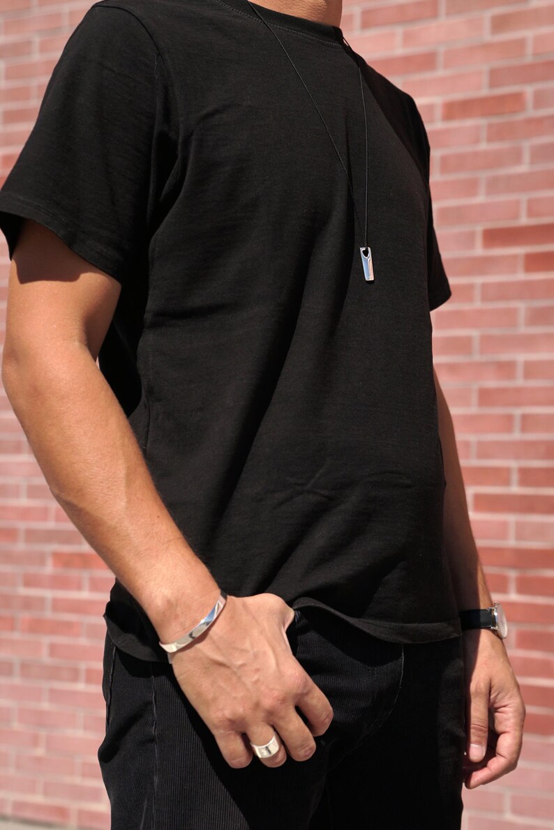 A man wearing a black shirt and jeans, showcasing a stylish polished silver bar necklace as a modern accessory.