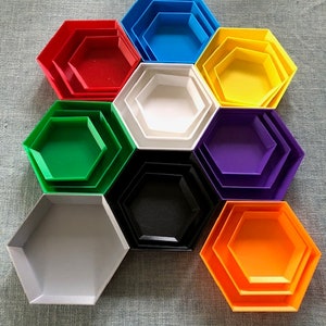 Könnte beinhalten: Ein Satz von zehn hexagonalen, ineinander verschachtelten Tabletts in verschiedenen Farben, darunter Rot, Blau, Grün, Lila, Schwarz, Weiß und Orange. Die Tabletts sind in einem Kreis angeordnet, wobei das größte Tablett unten und das kleinste Tablett oben liegt.
