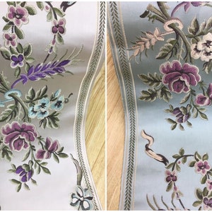 Op de afbeelding: Twee voorbeelden van geborduurde bies met een bloemenmotief. De bies aan de linkerkant is op een witte achtergrond en de bies aan de rechterkant is op een lichtblauwe achtergrond.