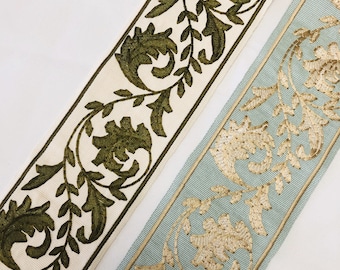 Pode incluir: Duas fitas de guarnição bordadas, uma com um desenho floral verde sobre fundo branco e a outra com um desenho floral dourado sobre fundo azul claro.