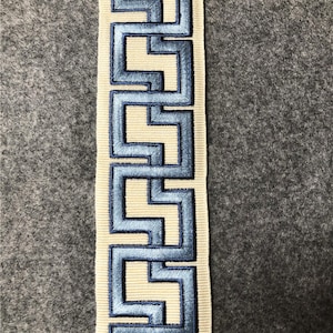 May include: A white ribbon with a blue geometric pattern. The pattern is a repeating design of interlocking squares and rectangles.