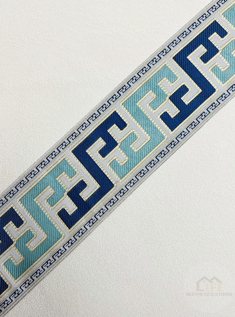 Pode incluir: Trimming azul e branco com um padr&atilde;o geom&eacute;trico. O trimming apresenta um desenho repetitivo de quadrados com um motivo de chave grega.