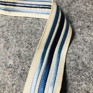 May include: A beige ribbon with blue and navy stripes. The ribbon is woven with a subtle texture.