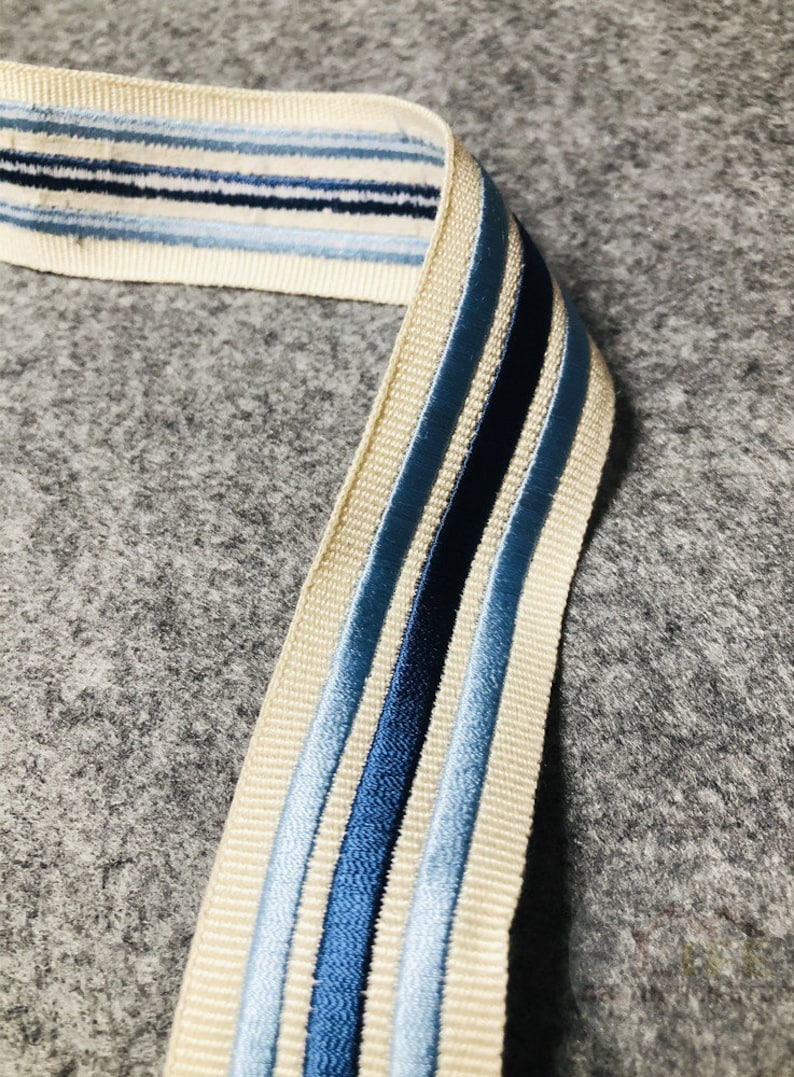 May include: A beige ribbon with blue and navy stripes. The ribbon is woven with a subtle texture.