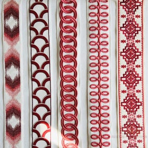 May include: Close-up of five decorative ribbons with various red and white patterns. Designs include geometric shapes, interlocking circles, and embroidered floral motifs. The ribbons are displayed vertically against a white background.