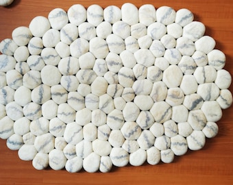 May include: A white and gray oval-shaped rug made of felt stones. The rug is made up of many small, round stones that are sewn together.