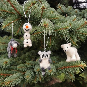 Op de afbeelding: Vier vilten ornamenten hangen aan een groene kerstboom. De ornamenten zijn een sneeuwpop, een wasbeer, een ezel en een ijsbeer.