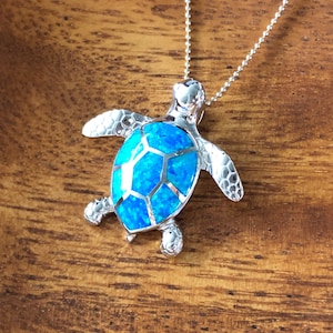 May include: A silver necklace with a blue opal turtle pendant. The turtle is detailed with a textured shell and has a silver chain.