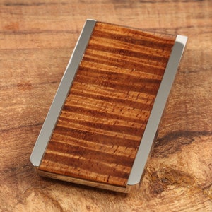 May include: A rectangular money clip with a polished silver frame and a rich, textured wood grain center. The wood has a warm, reddish-brown hue with darker streaks, creating a natural, elegant look. The clip is designed to hold currency and cards.