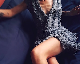 May include: A gray crocheted dress with fringe detailing. The dress is worn by a person lying on a blue surface.