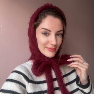 May include: A woman wearing a burgundy fuzzy scarf tied in a bow around her neck. She is wearing a black and white striped sweater.