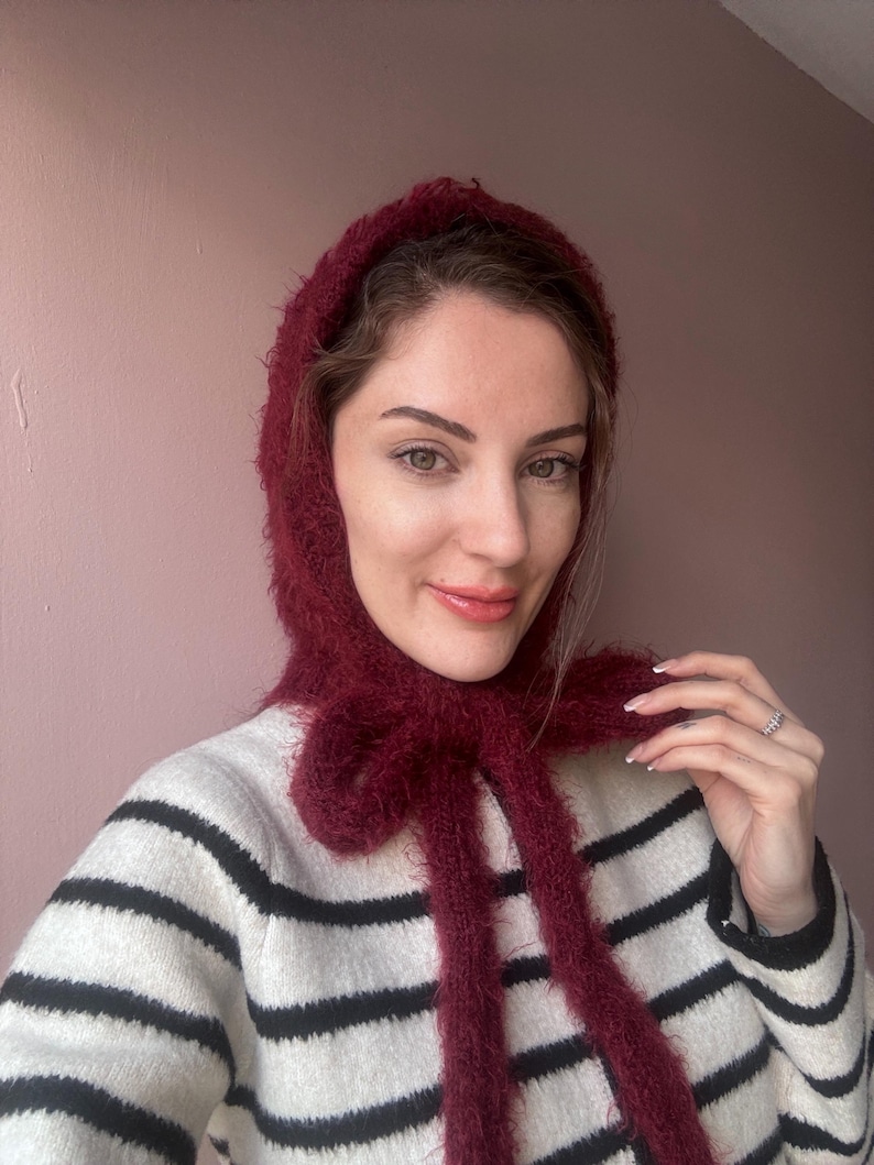 May include: A woman wearing a burgundy fuzzy scarf tied in a bow around her neck. She is wearing a black and white striped sweater.
