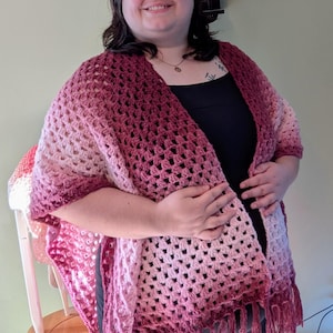 Peut inclure: Un châle en crochet fait à la main, à tissage ouvert, dans les tons de rose et de bordeaux. Le châle présente un bord à franges et un motif de couleur dégradé, passant du rose clair au bordeaux foncé. Cette écharpe confortable est parfaite.