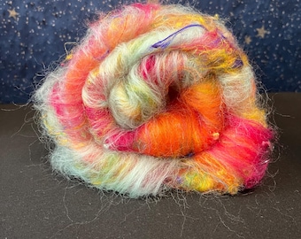 May include: A colorful ball of yarn with shades of pink, orange, yellow, green, and blue. The yarn is rolled up and has a fluffy texture.