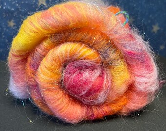 May include: A ball of yarn in shades of pink, orange, and yellow with iridescent fibers woven throughout. The yarn is rolled into a spiral shape.