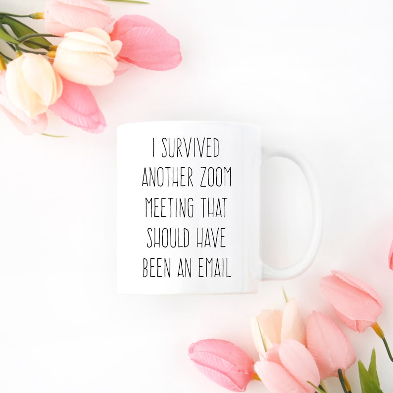 Pu&ograve; includere: Una tazza in ceramica bianca con testo nero che recita "Sono sopravvissuto a un'altra riunione Zoom che avrebbe dovuto essere un'e-mail". La tazza &egrave; circondata da fiori rosa.