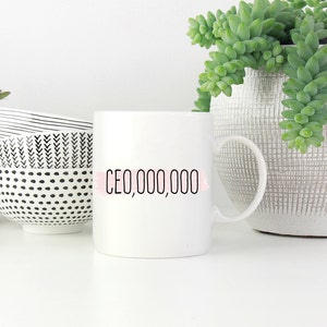 Op de afbeelding: Witte keramische mok met zwarte tekst die "CEO,000,000" luidt met een roze aquarelstreep achter de tekst.