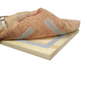 May include: A close-up of a light brown fabric with two strips of gray adhesive tape attached to it. The fabric is being peeled back to reveal a wooden board with a gray adhesive tape border.