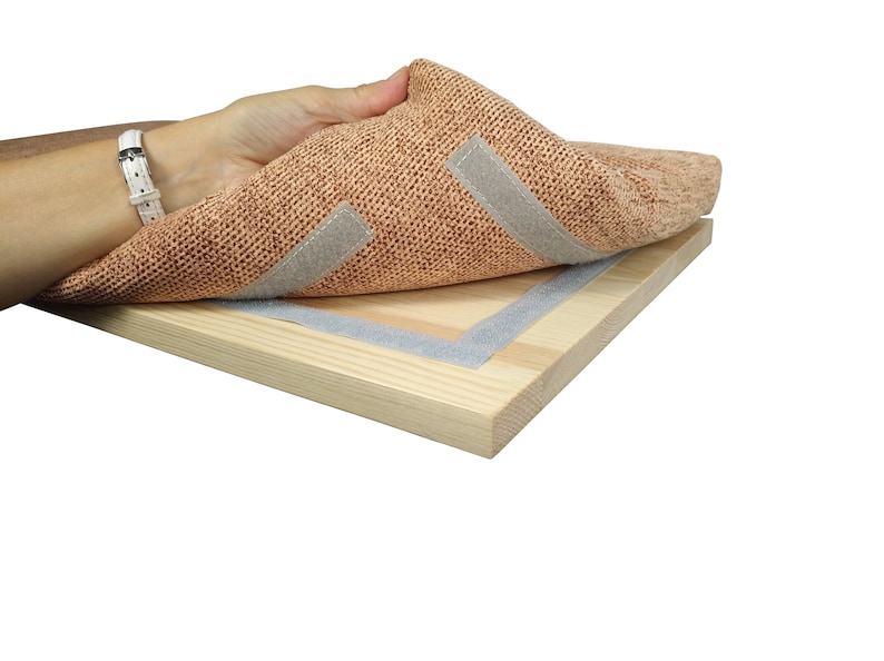 May include: A close-up of a light brown fabric with two strips of gray adhesive tape attached to it. The fabric is being peeled back to reveal a wooden board with a gray adhesive tape border.