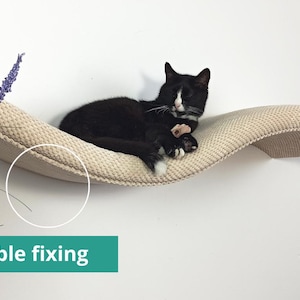 May include: A wall-mounted cat shelf with a curved, wave-like design and a textured, beige fabric surface. A black and white cat is resting on the shelf. The product features an invisible fixing system as indicated by the text on the image.