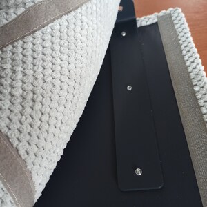 May include: A textured light gray fabric panel with a beige border, partially folded back to reveal a smooth black interior panel. The black panel features a vertical strip with three evenly spaced silver-toned metal rivets or fasteners.